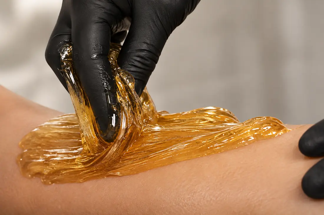 Warm sugar paste being worked across the skin by a gloved hand